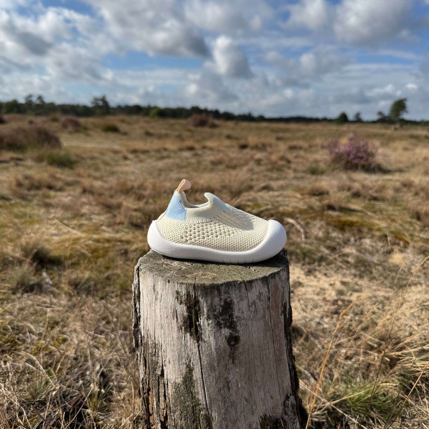 Beige kindersokschoen met antislip zool en flexibele pasvorm op een boomstronk in de natuur