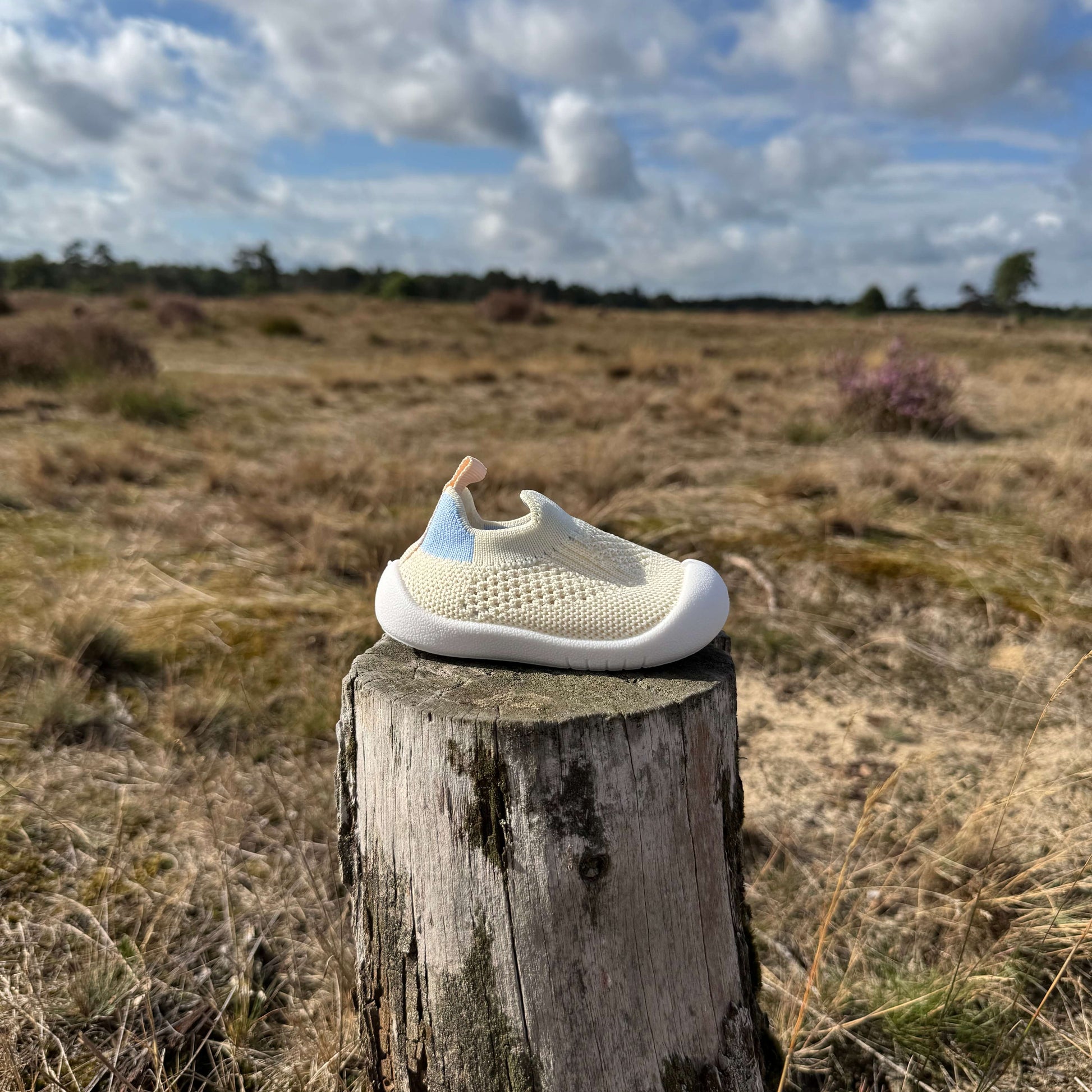 Beige kindersokschoen met antislip zool en flexibele pasvorm op een boomstronk in de natuur