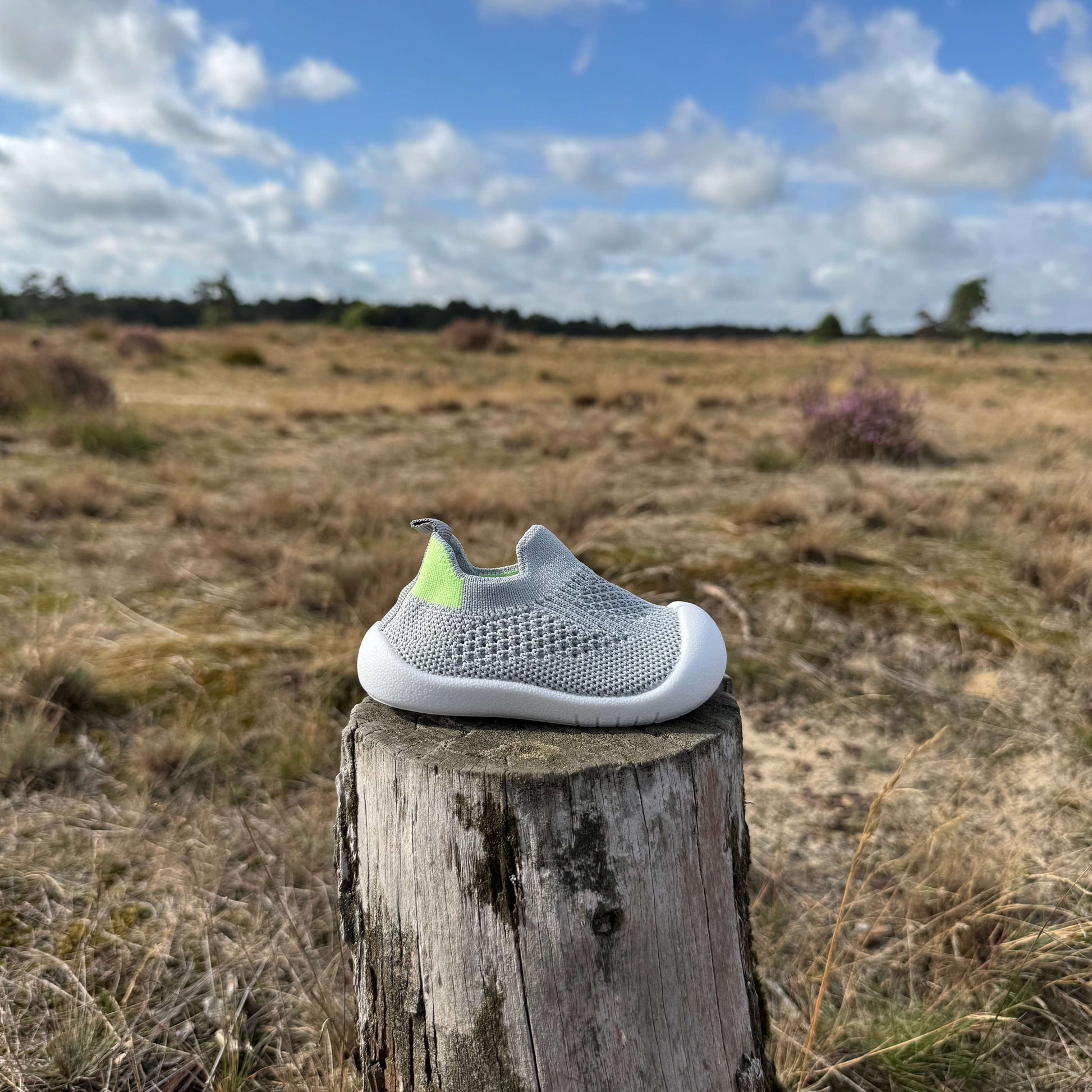 Grijze kindersokschoen met antislip zool en flexibele pasvorm op een boomstronk in de natuur