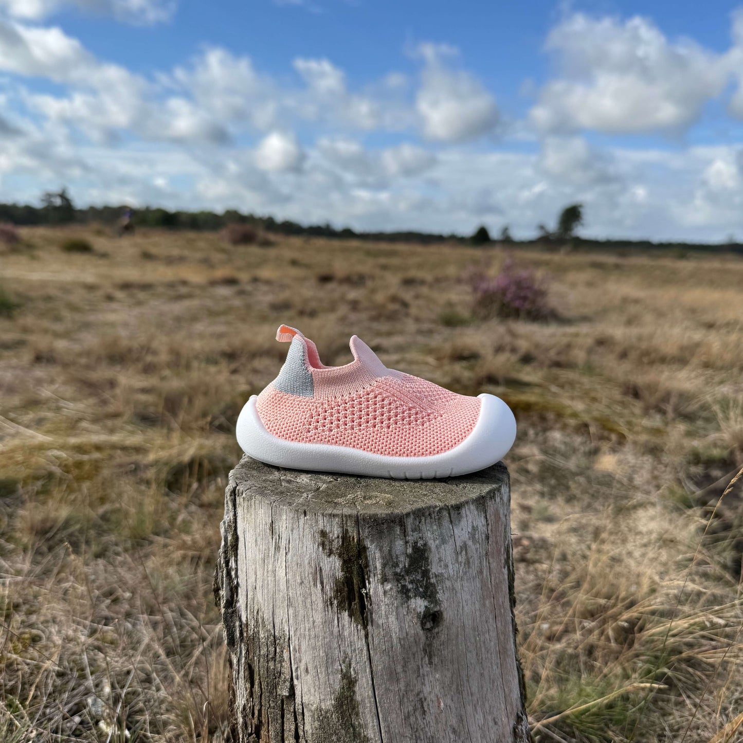 Roze kindersokschoen met antislip zool en flexibele pasvorm op een boomstronk in de natuur